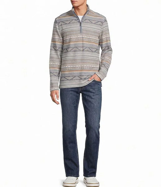 A man wearing a long-sleeve quarter-zip pullover sweater with a gray, beige, and brown geometric pattern, paired with dark blue jeans and white sneakers, against a plain white background.