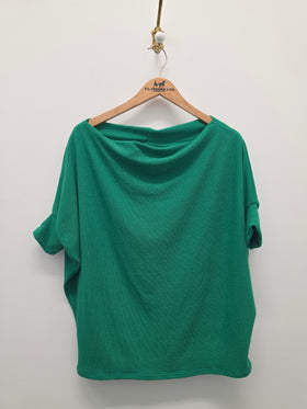 A green short-sleeve top with a draped, wide neckline hanging on a wooden hanger against a plain white wall.