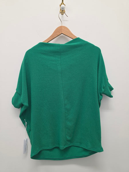 A green short-sleeve top hanging on a wooden hanger against a plain white wall, showing the back view of the garment.