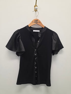 A black short-sleeve blouse with sheer flutter sleeves and a button-front neckline, hanging on a wooden hanger against a plain light wall.