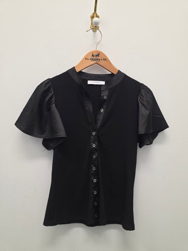 A black short-sleeve blouse with sheer flutter sleeves and a button-front neckline, hanging on a wooden hanger against a plain light wall.