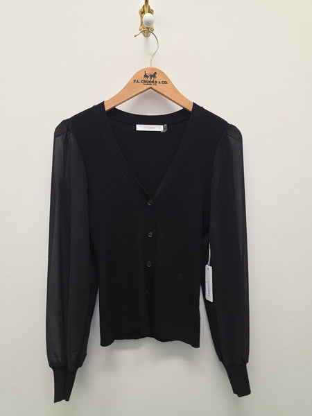 A black long-sleeve cardigan sweater with sheer mesh sleeves, hanging on a wooden hanger against a plain off-white wall.