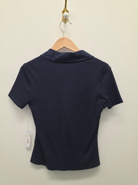 A navy blue short-sleeve polo shirt shown from the back, hanging on a wooden hanger against a plain off-white wall.