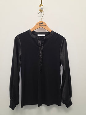 A black long-sleeve blouse with a satin-like button placket and round neckline, hanging on a wooden hanger against a plain light wall.