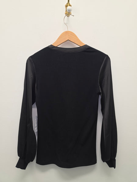 A black long-sleeve blouse  hanging on a wooden hanger against a plain light wall.