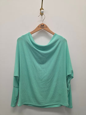 A mint green long-sleeve top with a wide draped neckline, hanging on a wooden hanger against a plain light gray wall.