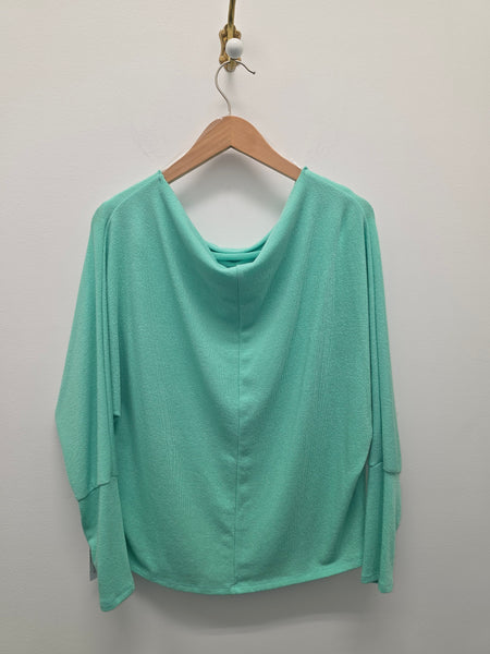 A mint green long-sleeve top with a draped, wide neckline, hanging on a wooden hanger against a plain light gray wall.
