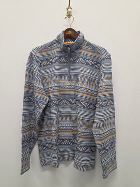 A long-sleeve quarter-zip pullover sweater with a blue, beige, and white geometric pattern, hanging on a wooden hanger against a plain off-white wall.