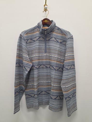 A long-sleeve quarter-zip pullover sweater with a blue, beige, and white geometric pattern, hanging on a wooden hanger against a plain off-white wall.