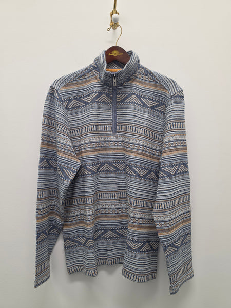 A long-sleeve quarter-zip pullover sweater with a blue, beige, and white geometric pattern, hanging on a wooden hanger against a plain off-white wall.
