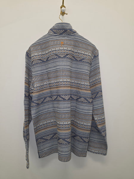 A long-sleeve quarter-zip pullover sweater with a blue, beige, and white geometric pattern, hanging on a wooden hanger against a plain off-white wall.