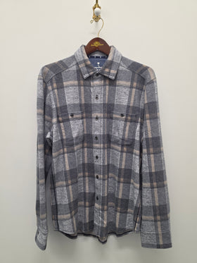 A gray and beige plaid long-sleeve button-up shirt hanging on a wooden hanger against a plain off-white wall.