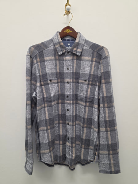A gray and beige plaid long-sleeve button-up shirt hanging on a wooden hanger against a plain off-white wall.