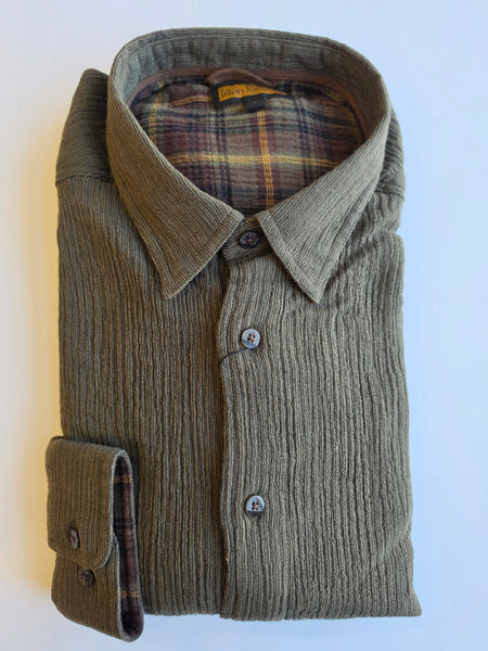 A folded long-sleeve button-up shirt in a textured olive green corduroy-like fabric, showing a plaid lining in brown, red, and yellow tones. The shirt is neatly folded on a plain white background.