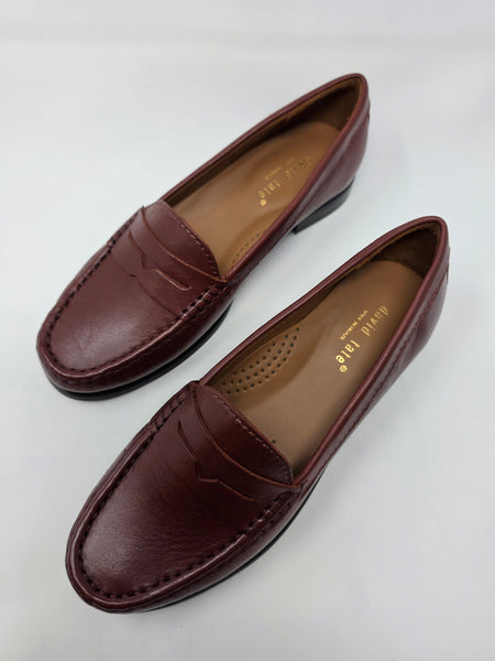 A pair of women's penny loafers in a deep burgundy-brown leather, displayed on a clean white background. The shoes feature a low block heel and are shown from both the side and top-down angles, revealing a tan insole with the brand name 'david jase' printed in gold.