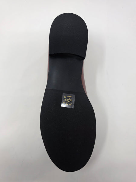 The black rubber outsole of a shoe, showing a small gold and silver brand label near the center, photographed from a top-down view on a white background.