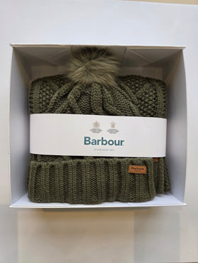 An olive green Barbour cable-knit beanie with a matching pom-pom, presented inside its white gift box with a white paper band.