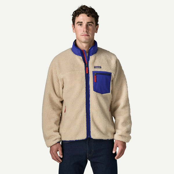 A man wearing a Patagonia fleece jacket in beige with royal blue collar, zipper placket, and chest pocket, paired with dark blue jeans, against a light gray studio background.
