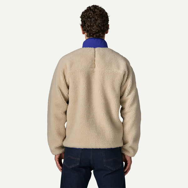 A man viewed from behind wearing a beige sherpa fleece pullover with a contrasting blue collar, paired with dark blue jeans, against a light off-white background.