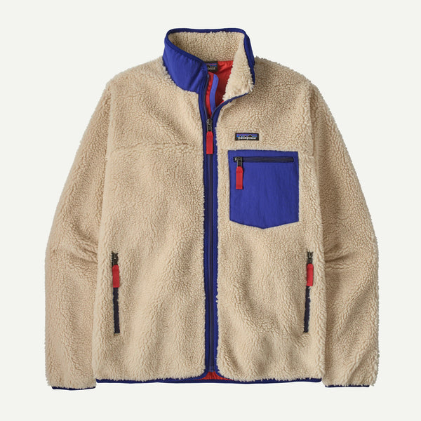 A Patagonia fleece jacket in beige with royal blue and red accents, featuring a stand-up collar, a chest pocket, and zippered hand pockets, shown against a plain white background.