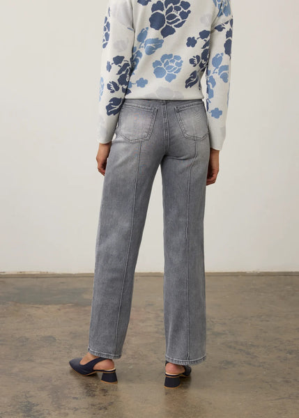 A person shown from the back wearing light gray wide-leg jeans, a white long-sleeve top with blue floral print, and dark heeled sandals in a studio setting.