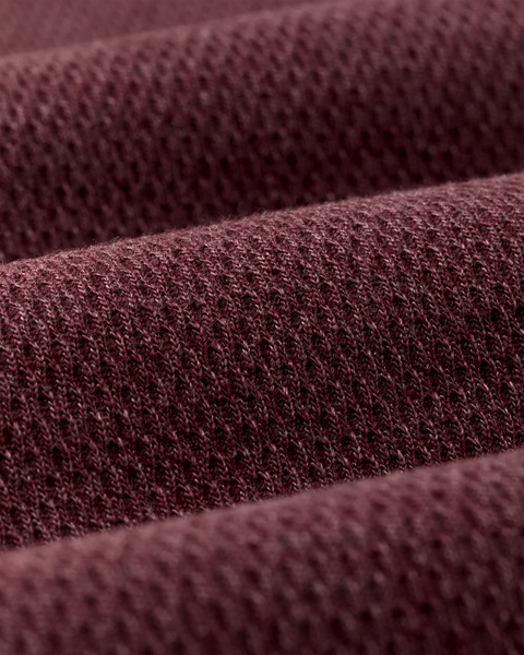A close-up of textured knit fabric in a deep burgundy or maroon shade, shown with soft folds and a fine woven pattern.