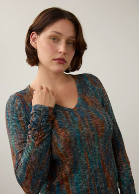 A woman wearing a long-sleeve V-neck knit top with a textured, heathered pattern in teal blue, rust orange, and brown, posed against a neutral light gray background.