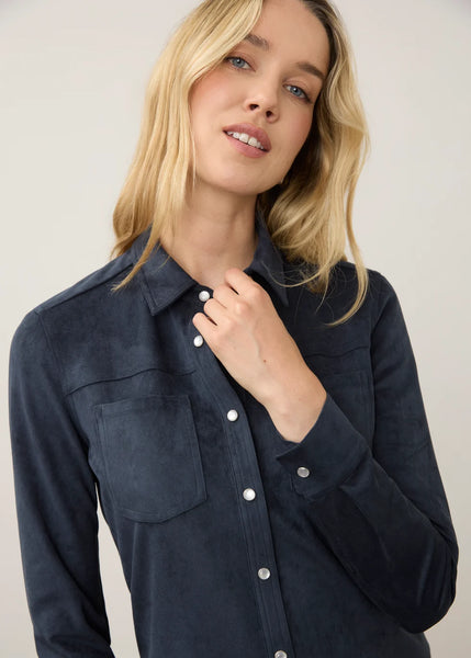 A woman wearing a dark navy blue long-sleeve button-up shirt with a collar and chest pocket, posed against a light gray studio background.