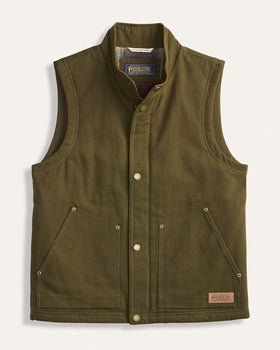 An olive green waxed canvas vest with a stand collar, snap-button front, and two front flap pockets, shown flat on a light cream background. The brand label 'Barbour' is visible inside the collar and on a small patch near the bottom right.