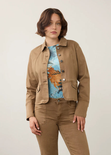 A woman modeling a cropped tan utility jacket over a blue and orange graphic t-shirt, paired with matching tan pants, against a plain light gray studio background.