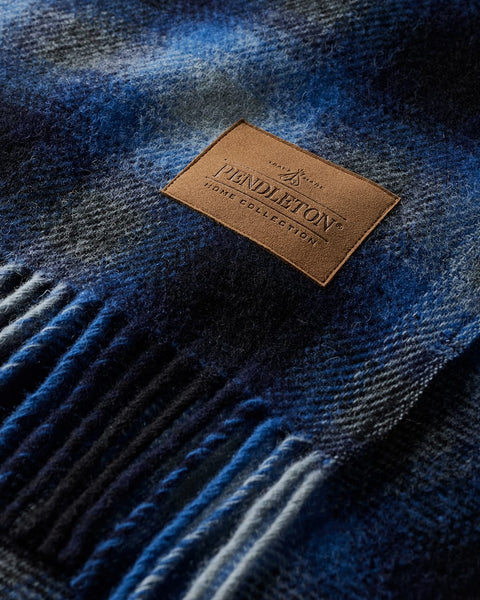 A close-up of a blue and navy plaid Pendleton wool blanket with a brown leather brand patch on the surface.