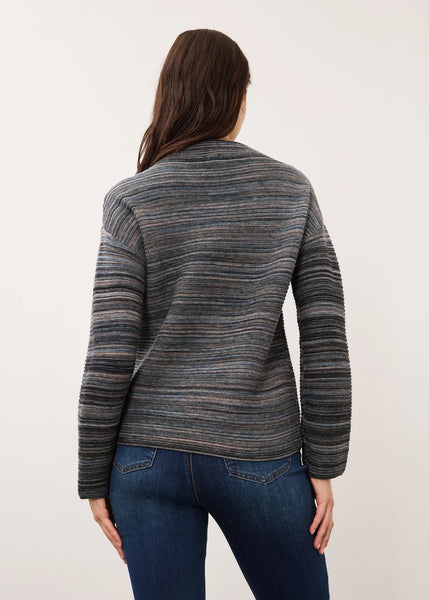 A woman viewed from the back wearing a long-sleeve knit sweater with horizontal gray, blue, and brown stripes, paired with dark blue jeans, against a plain off-white background.