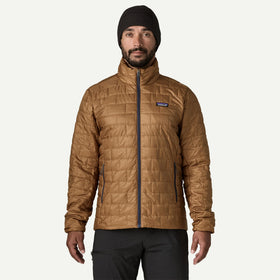 A man wearing a tan quilted Patagonia jacket, black beanie, and black pants, standing against a light gray background.