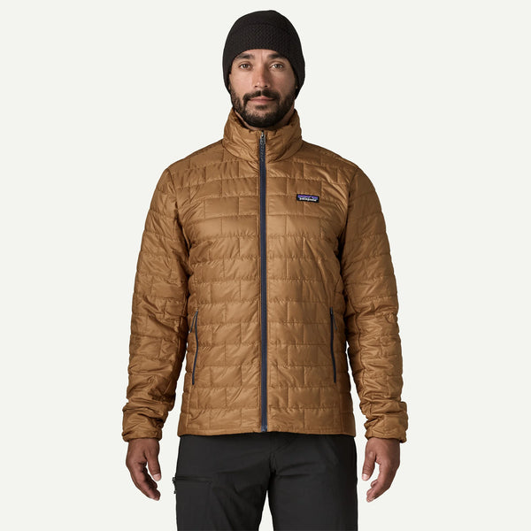 A man wearing a tan quilted Patagonia jacket, black beanie, and black pants, standing against a light gray background.