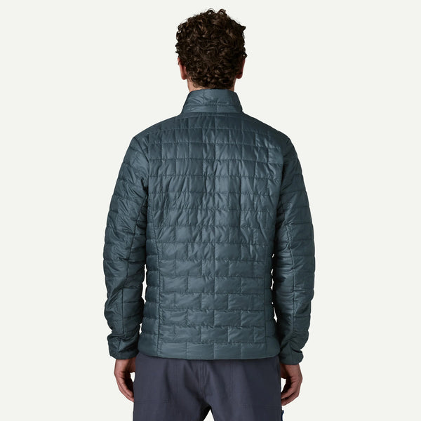 A man viewed from the back wearing a dark slate blue quilted puffer jacket and matching dark pants, set against a plain white background.