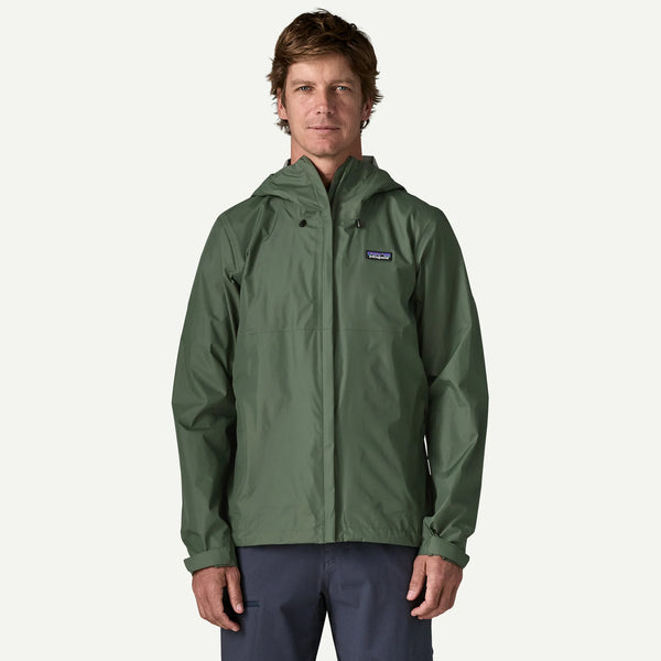 A man wearing a green Patagonia hooded rain jacket and navy pants, standing against a light gray studio background.