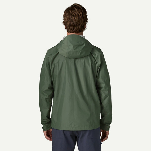 A man viewed from behind wearing an olive green hooded jacket and navy pants against a plain white background.