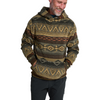 A smiling man wearing a patterned knit hoodie with geometric tribal-style designs in olive green, tan, brown, and rust orange, paired with dark pants, against a solid white background.