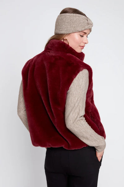 Woman wearing a red fur vest over a beige sweater on a white background