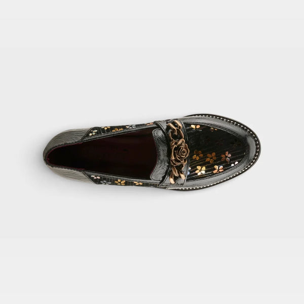 A single black patent leather loafer with a metallic rose detail on the strap and gold floral accents, shown from a top-down view on a light gray background.