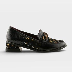 A single women's loafer-style shoe shown in side profile on a light gray studio background. The upper is primarily deep burgundy leather with a floral embroidered panel in black, pink, and white, plus a small gold-tone decorative accent near the vamp.