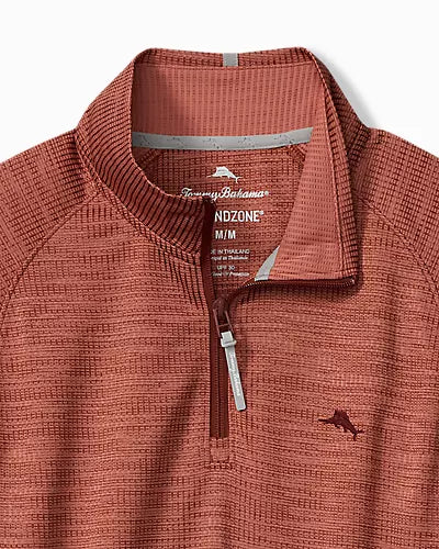 Close-up of a quarter-zip pullover top in a textured rust-orange fabric, featuring a stand collar, a silver zipper pull, and a small embroidered kangaroo logo on the left chest. The inner neck label shows the brand Tommy Hilfiger and the line Nozone.