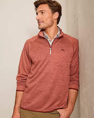 A man wearing a textured, heathered rust-colored quarter-zip pullover sweater with a small embroidered logo on the chest, layered over a patterned collared shirt.