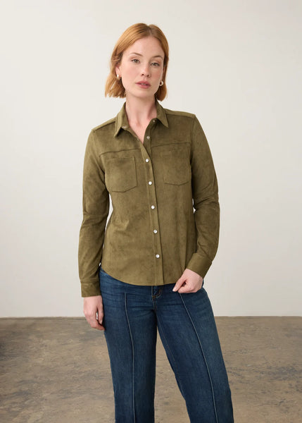 A woman modeling a long-sleeve button-up shirt in olive green suede-like fabric, paired with dark blue jeans, standing against a neutral studio backdrop.