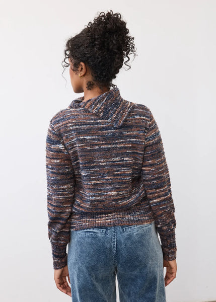 A person shown from the back wearing a marled knit sweater with horizontal stripes in navy, brown, beige, and muted orange, paired with blue jeans, against a plain white background.
