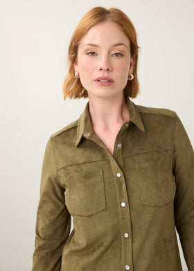 A woman with short auburn hair wearing an olive green suede button-up shirt, photographed against a plain off-white background.