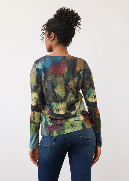 A woman viewed from behind wearing a long-sleeve top with an abstract multicolor print and blue jeans, standing against a plain light background.
