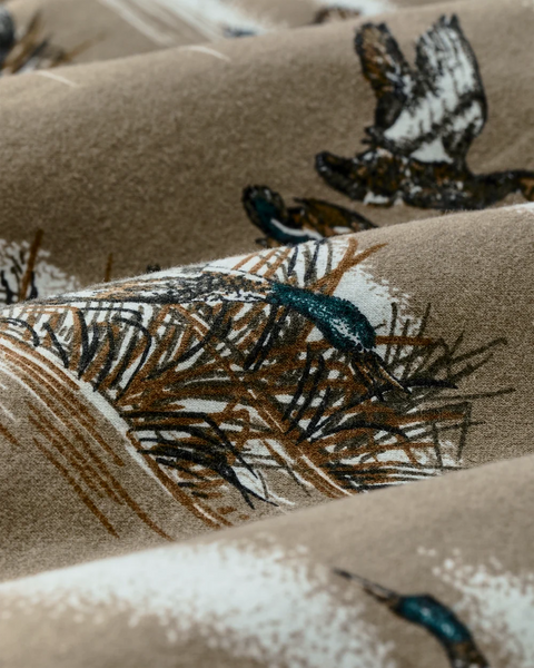 A close-up of a soft, draped fabric featuring a winter bird and pine branch pattern in brown, black, and white on a warm beige background.