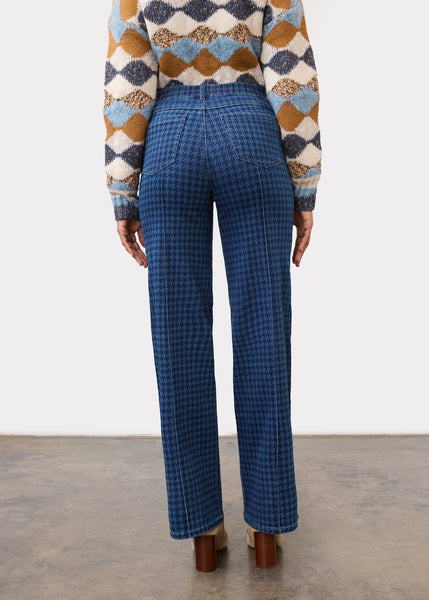 A person shown from the back wearing blue patterned wide-leg trousers and a multicolor diamond-pattern knit sweater, standing against a plain light wall.