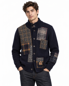 A man wearing a navy blue knit cardigan with large patchwork wool panels in herringbone and plaid patterns, paired with dark jeans against a plain white background.